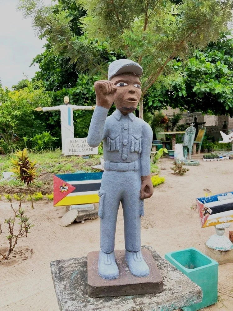 Blue cement soldier saluting, with Mozambican flag behind